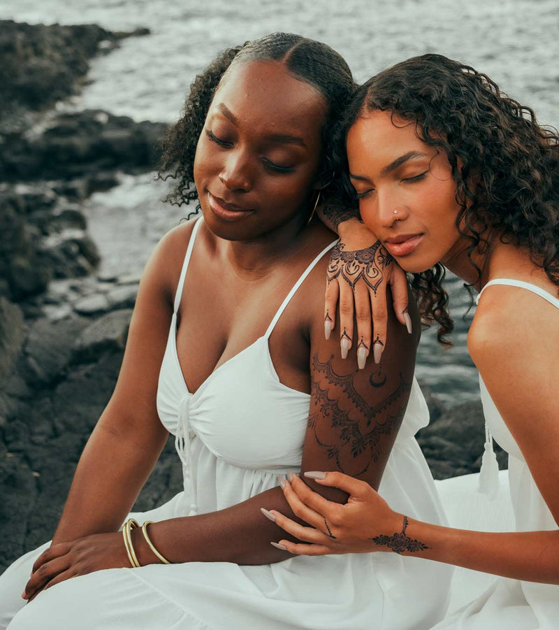Deux femmes portant des tatouages au jagua sur la plage, montrant des designs modernes et audacieux.